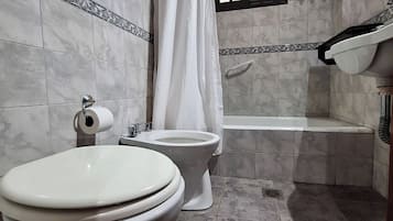Baño con dos inodoros, una bañera y una cortina de ducha.