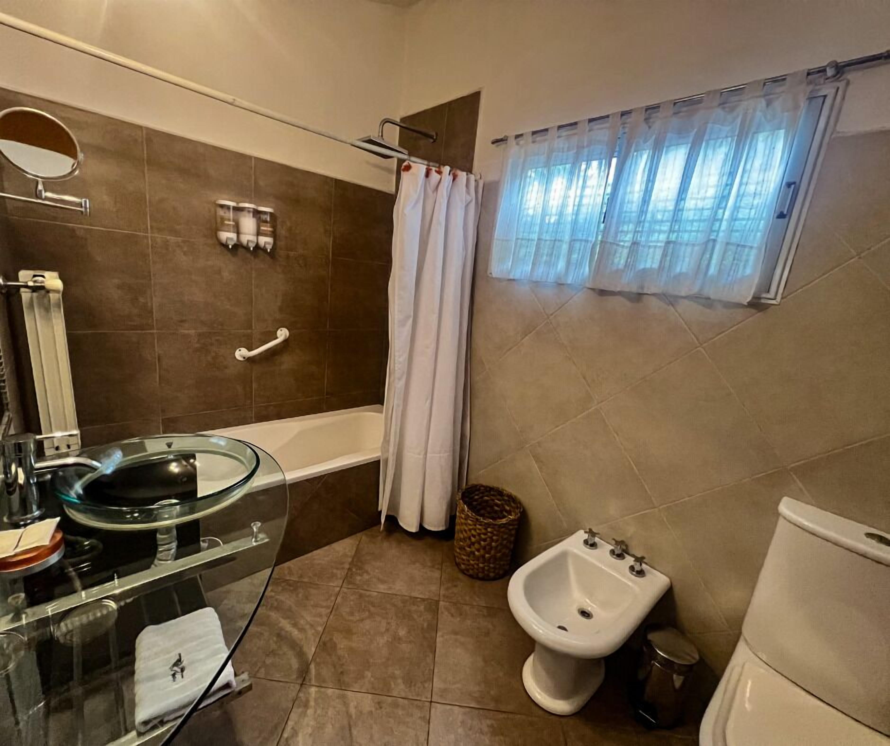Ein Badezimmer mit einem Glaswaschbecken, einem Bidet, einer Badewanne und einem Fenster mit Vorhang.