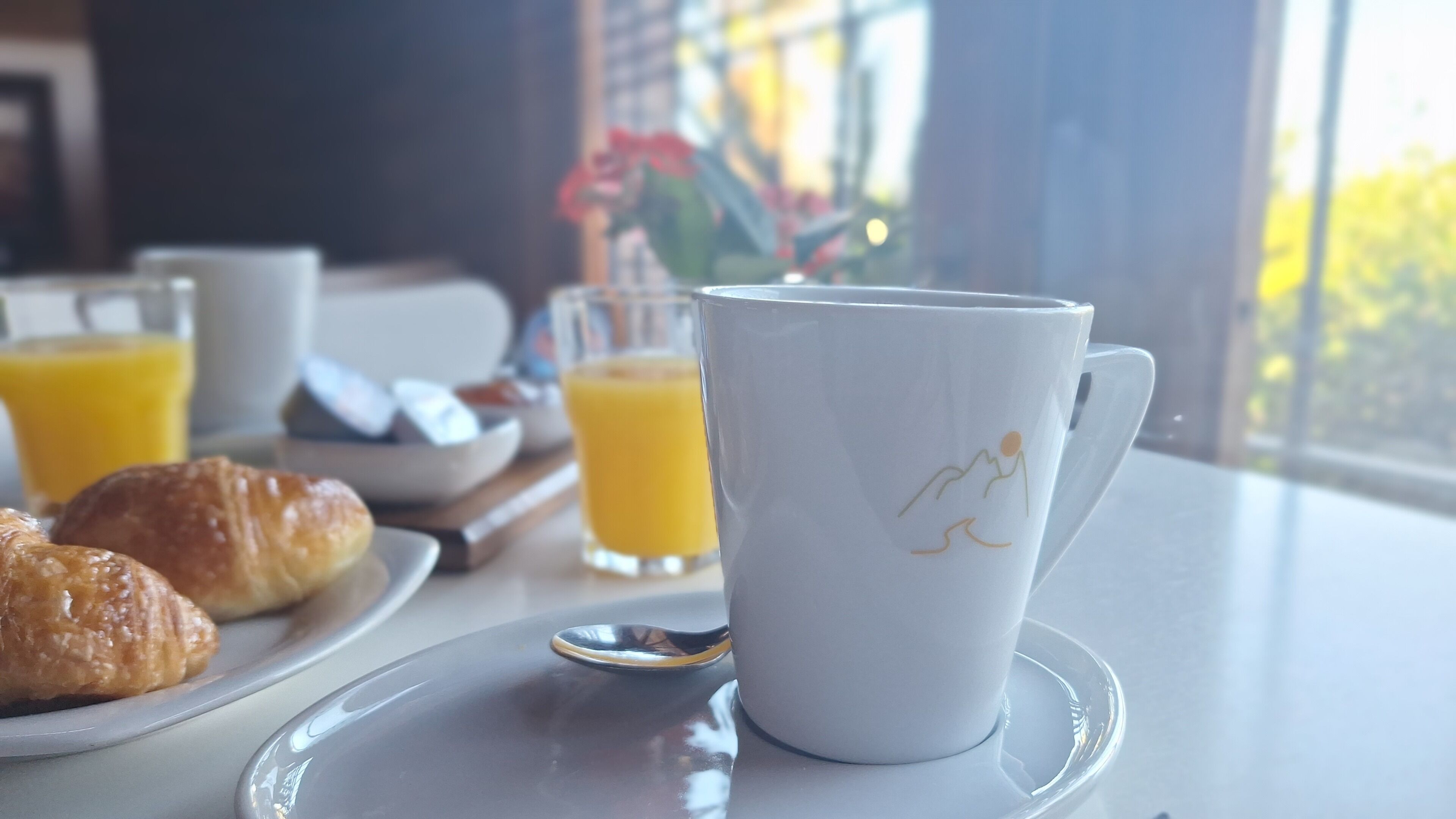 Een ontbijtsetting met croissants, sinaasappelsap en een witte mok op een tafel.