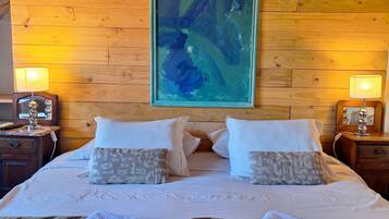 A hotel room with a wooden headboard, a large abstract painting, two bedside lamps, a bed with white linens, and two towels on the bed.