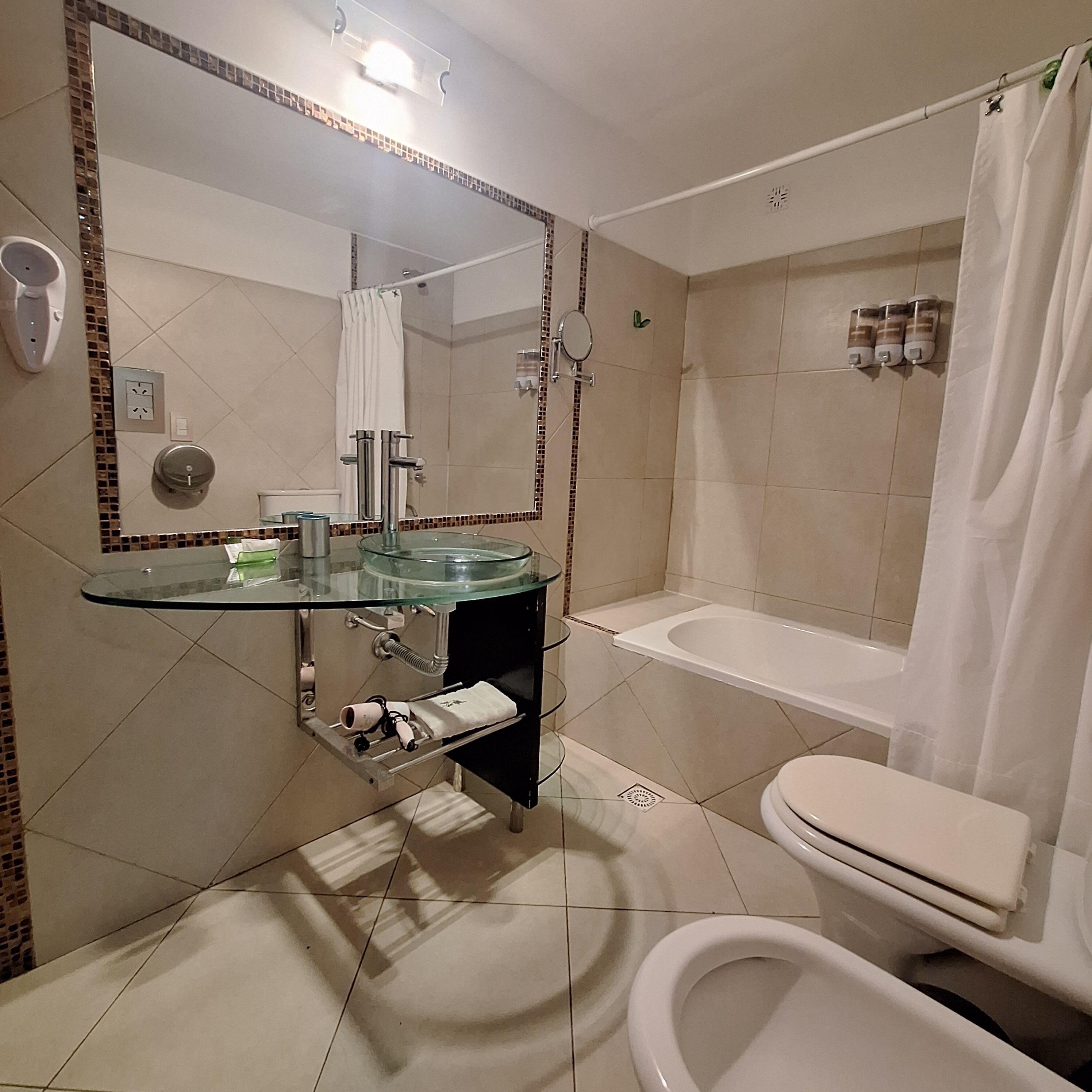 A bathroom with a glass sink, a toilet, a bathtub, and a shower.