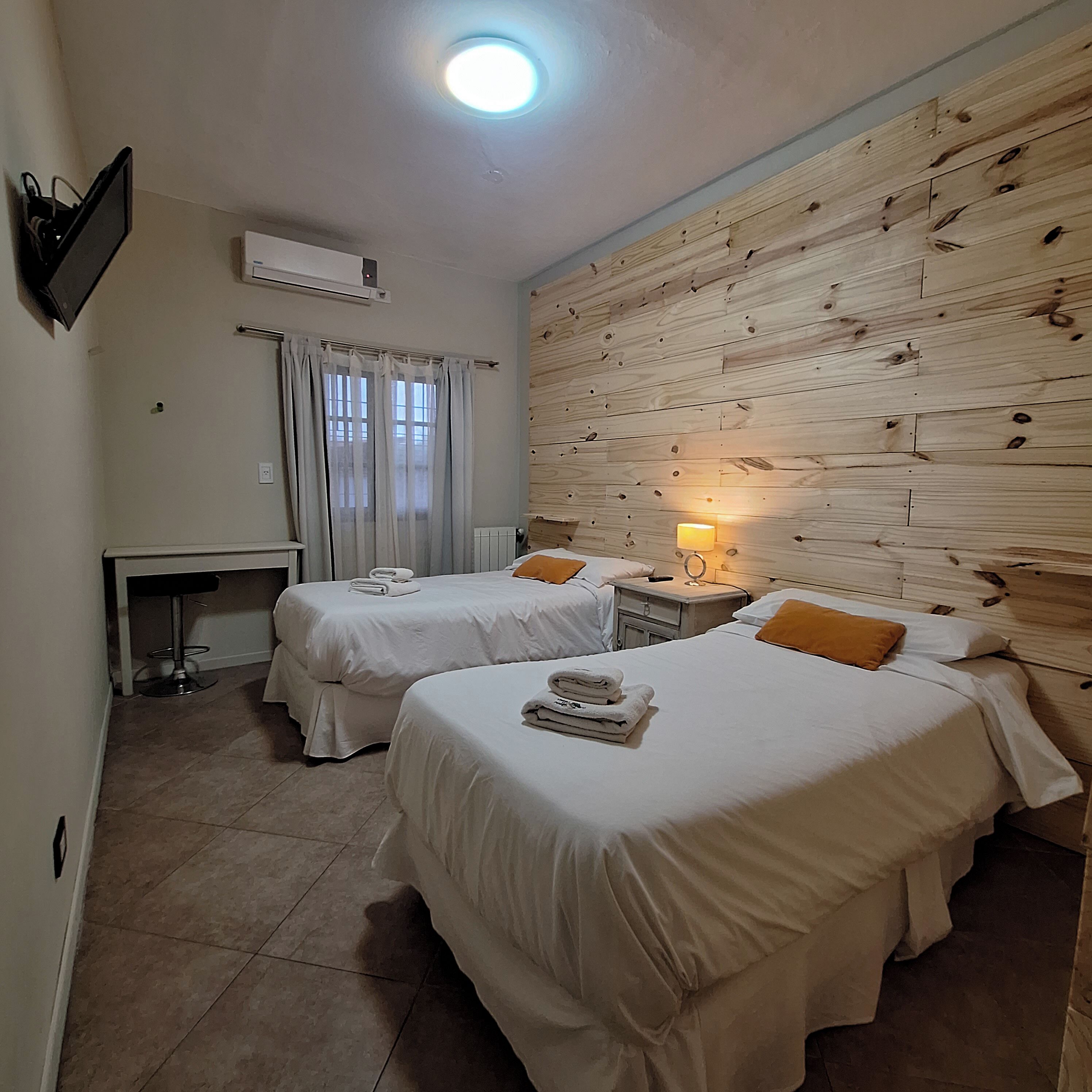 Een hotelkamer met twee bedden, een bureau, een stoel, een nachtkastje met lamp en een houten wand.