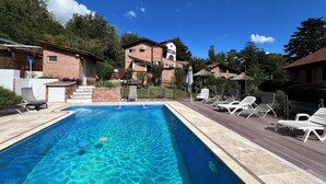 Una piscina rectangular con agua azul cristalina, rodeada por una terraza de madera con sillones de descanso.
