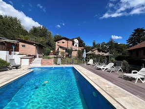 Une piscine rectangulaire Ă lâeau dâun bleu cristallin, entourĂ©e dâune terrasse en bois agrĂ©mentĂ©e de chaises longues.