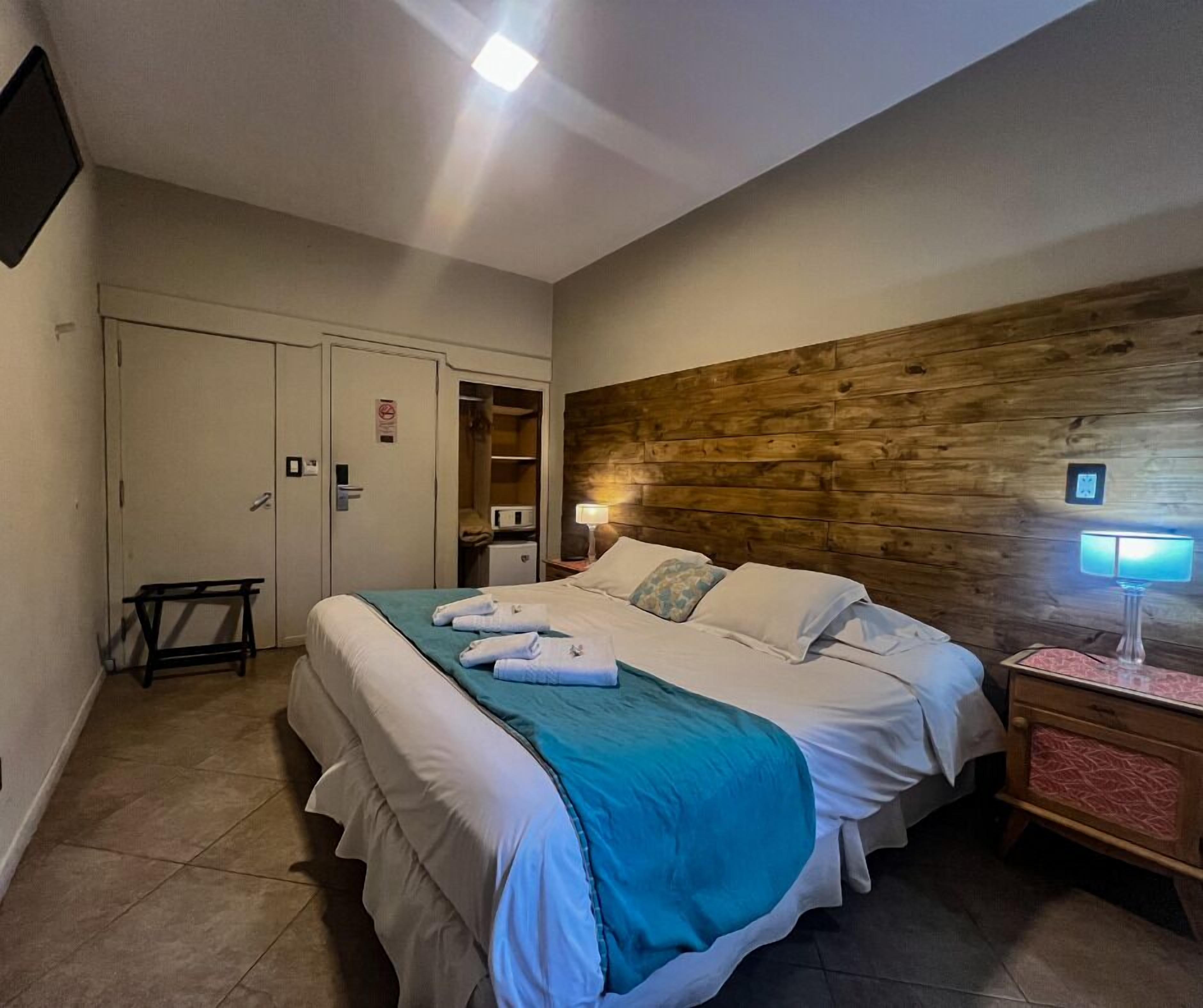 A hotel room with a bed, bedside table, lamp, and a wooden accent wall.