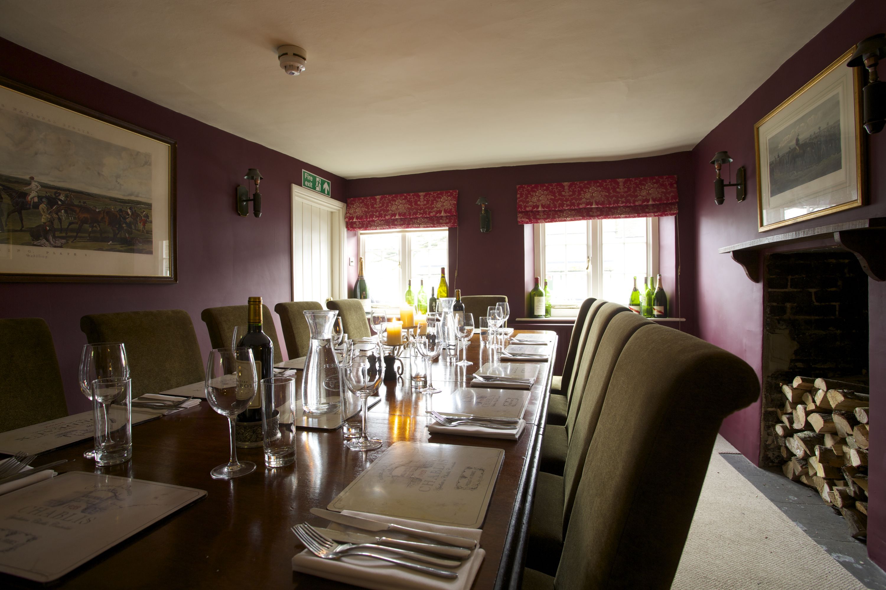 A dining room with a long table set for a meal, chairs, and a fireplace.