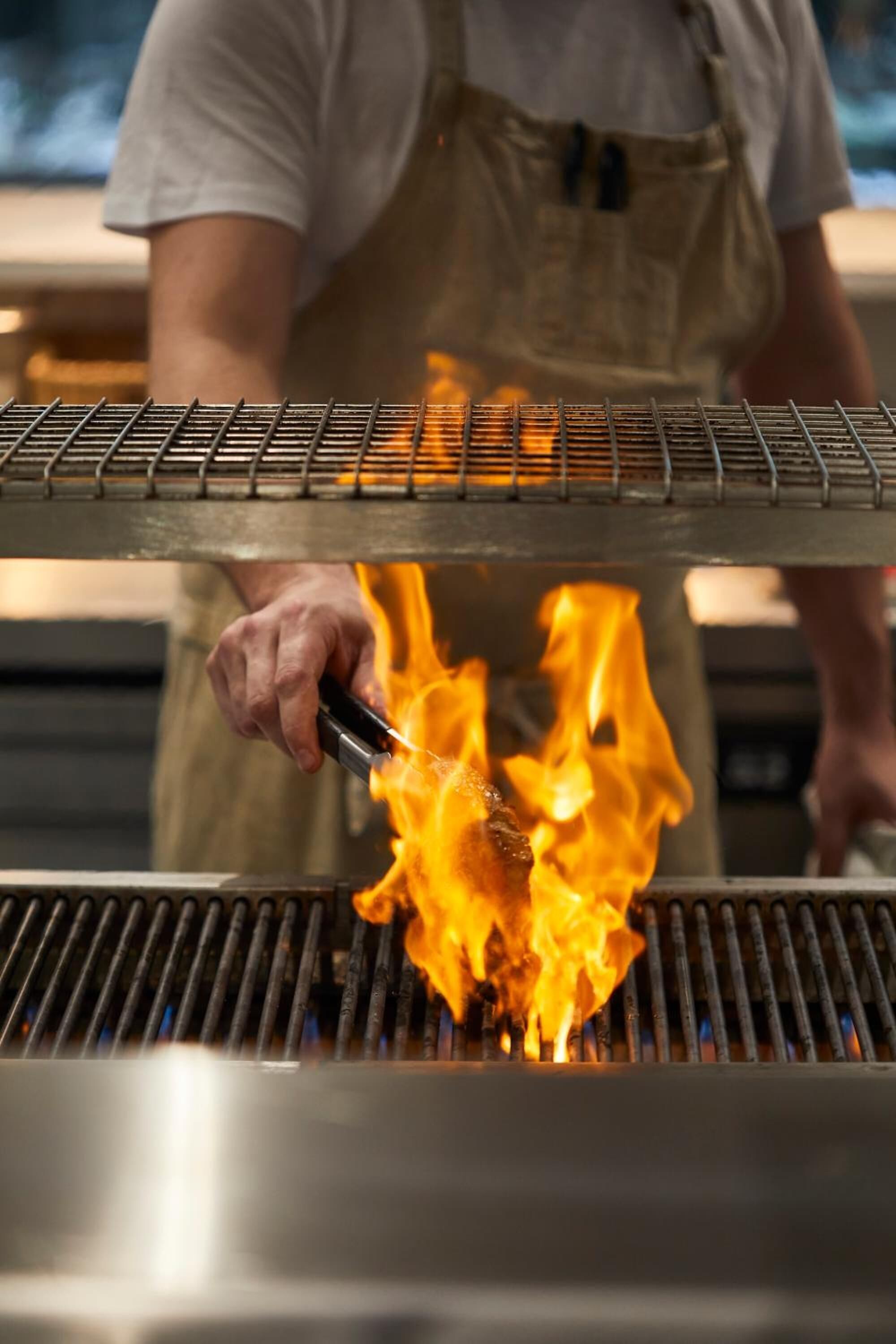 Eine Person grillt Fleisch über offenem Feuer.