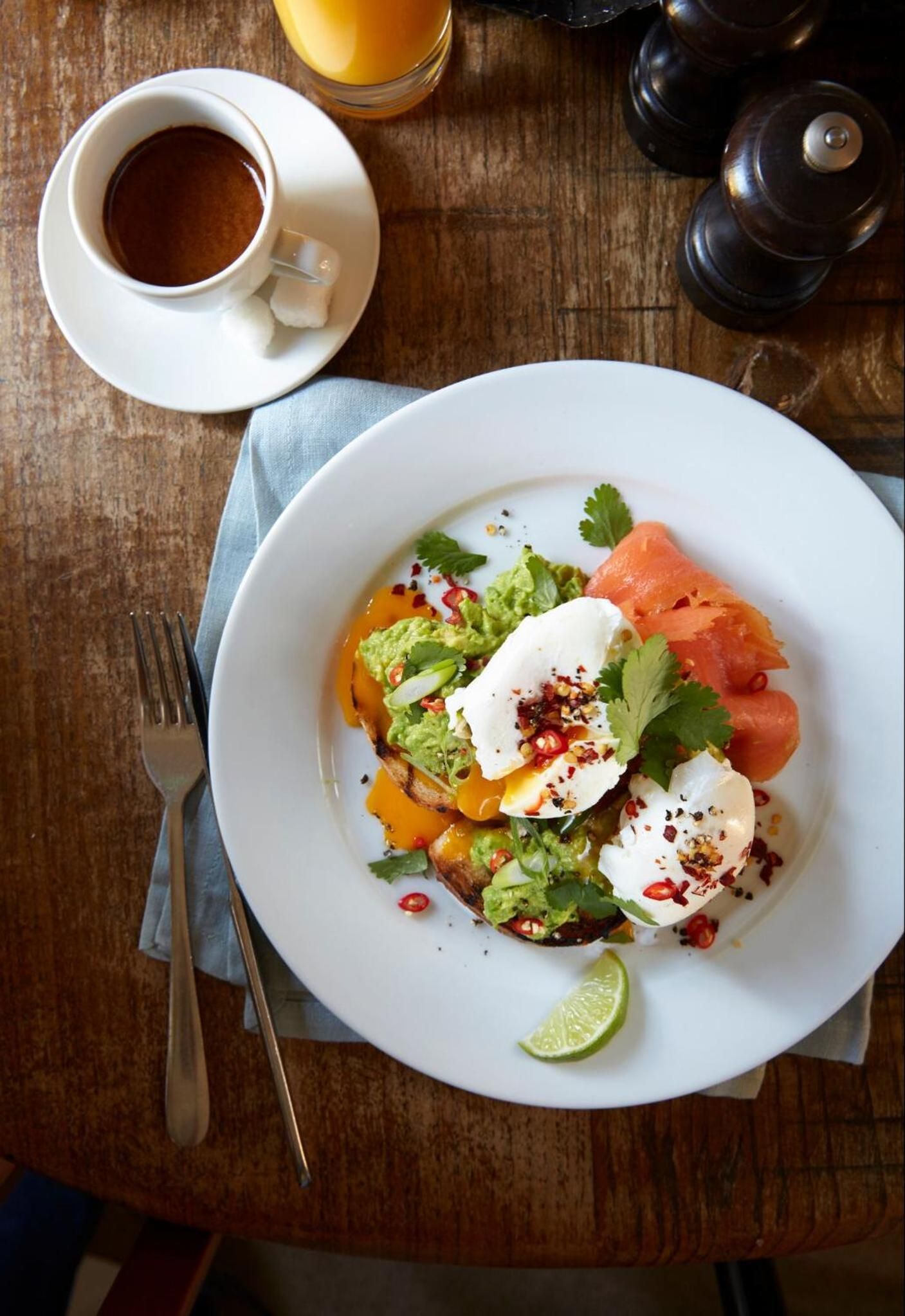 A plate of food with avocado, salmon, and a lime wedge on a wooden table.
