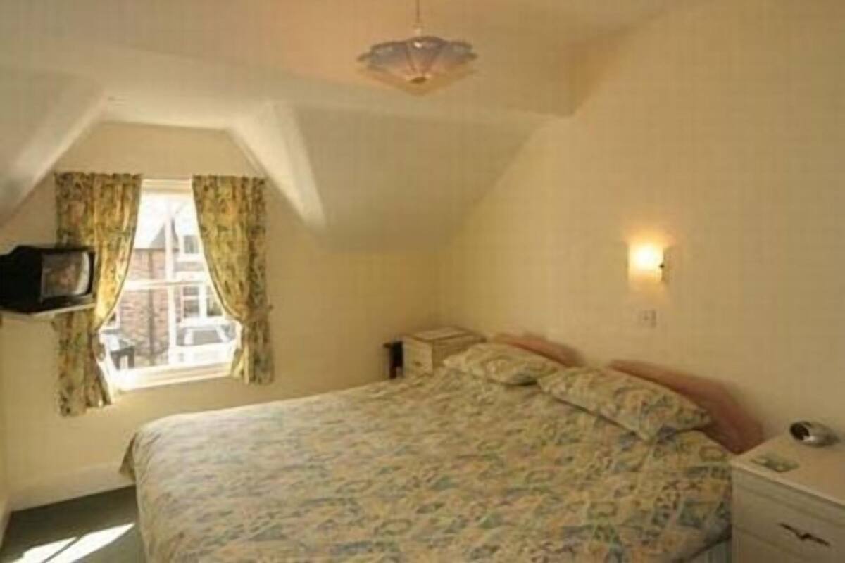 A bedroom with a bed, a window with curtains, a bedside table, and a wall-mounted light.