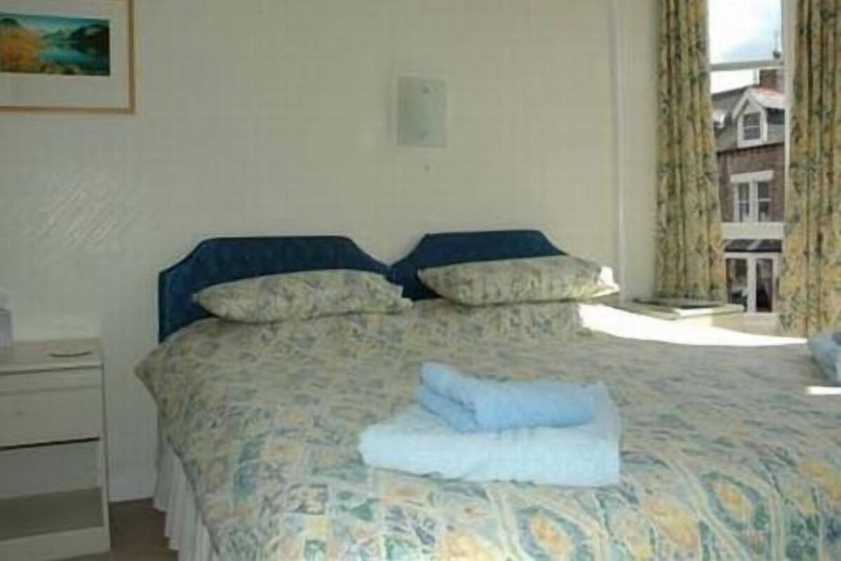 A bedroom with a bed, a bedside table, and a window with curtains.