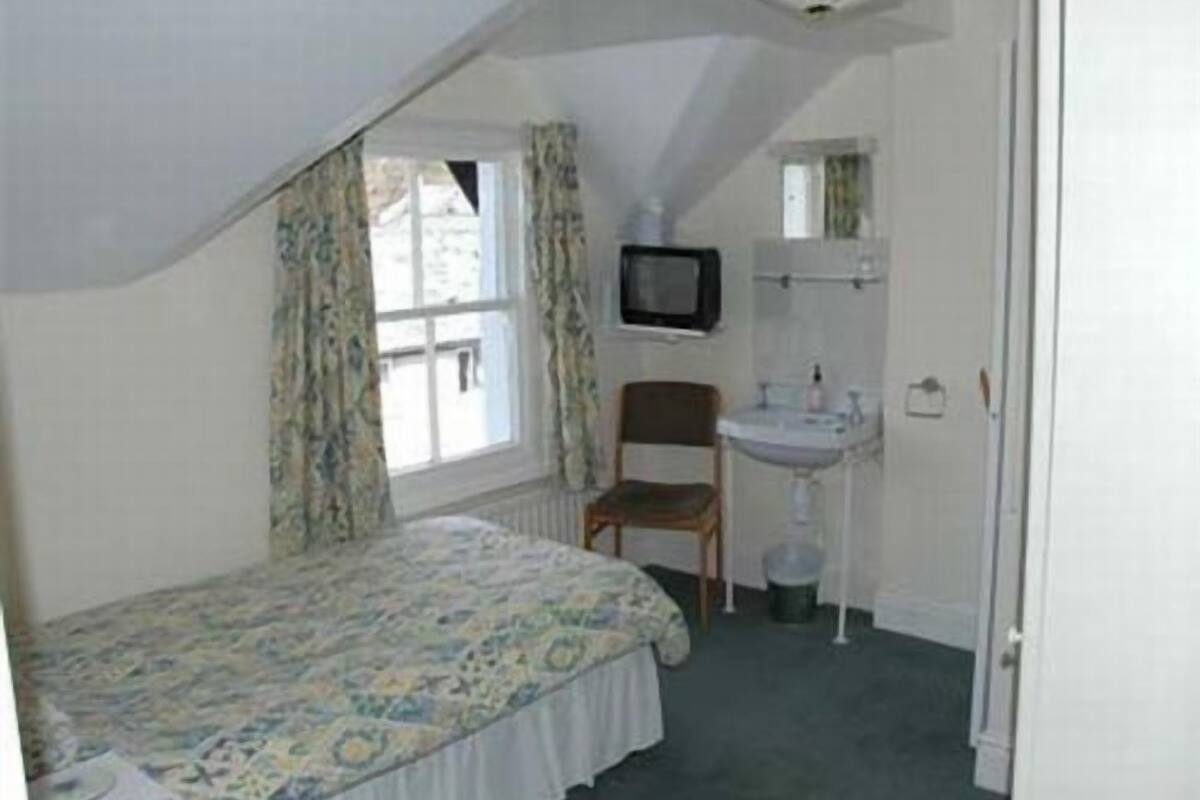 A bedroom with a bed, a chair, a television, and a sink.