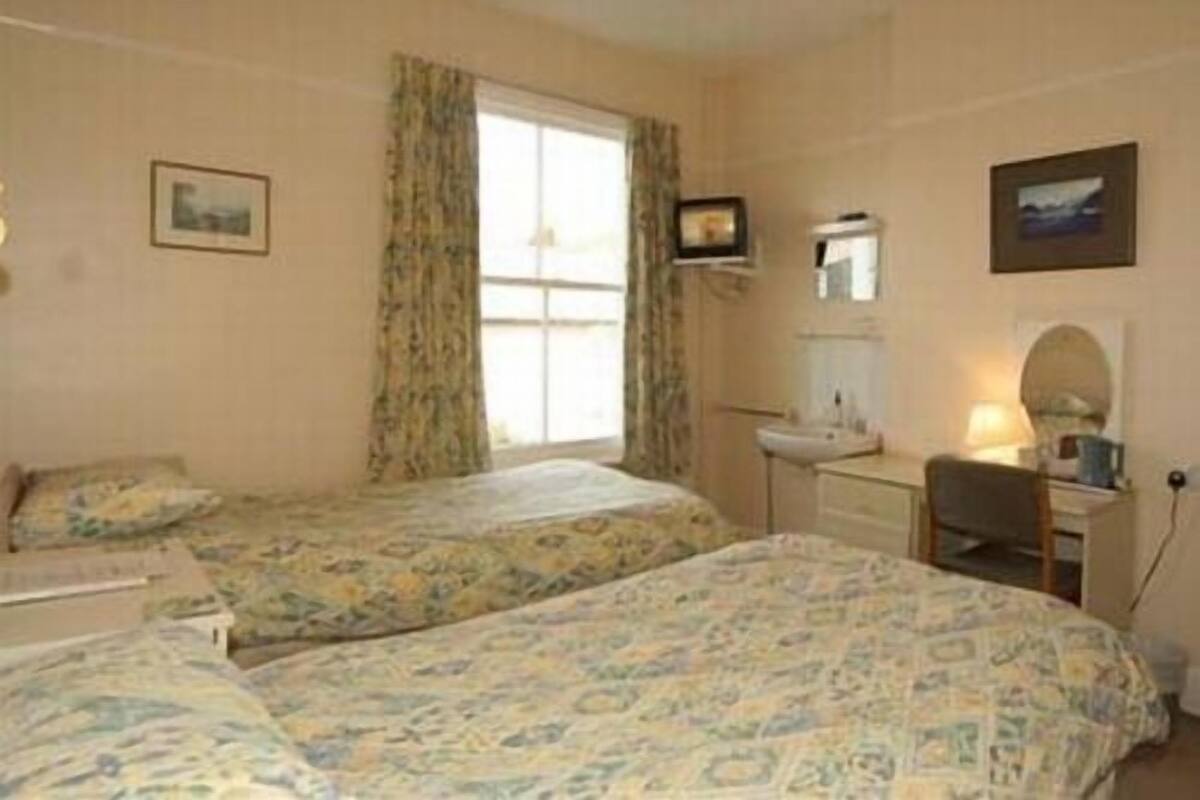 A bedroom with two beds, a desk, a chair, a window with curtains, and a wall-mounted mirror.
