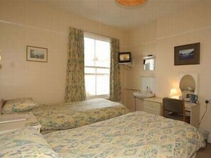 Une chambre avec deux lits, un bureau, une chaise, une fenêtre avec des rideaux et un miroir fixé au mur.