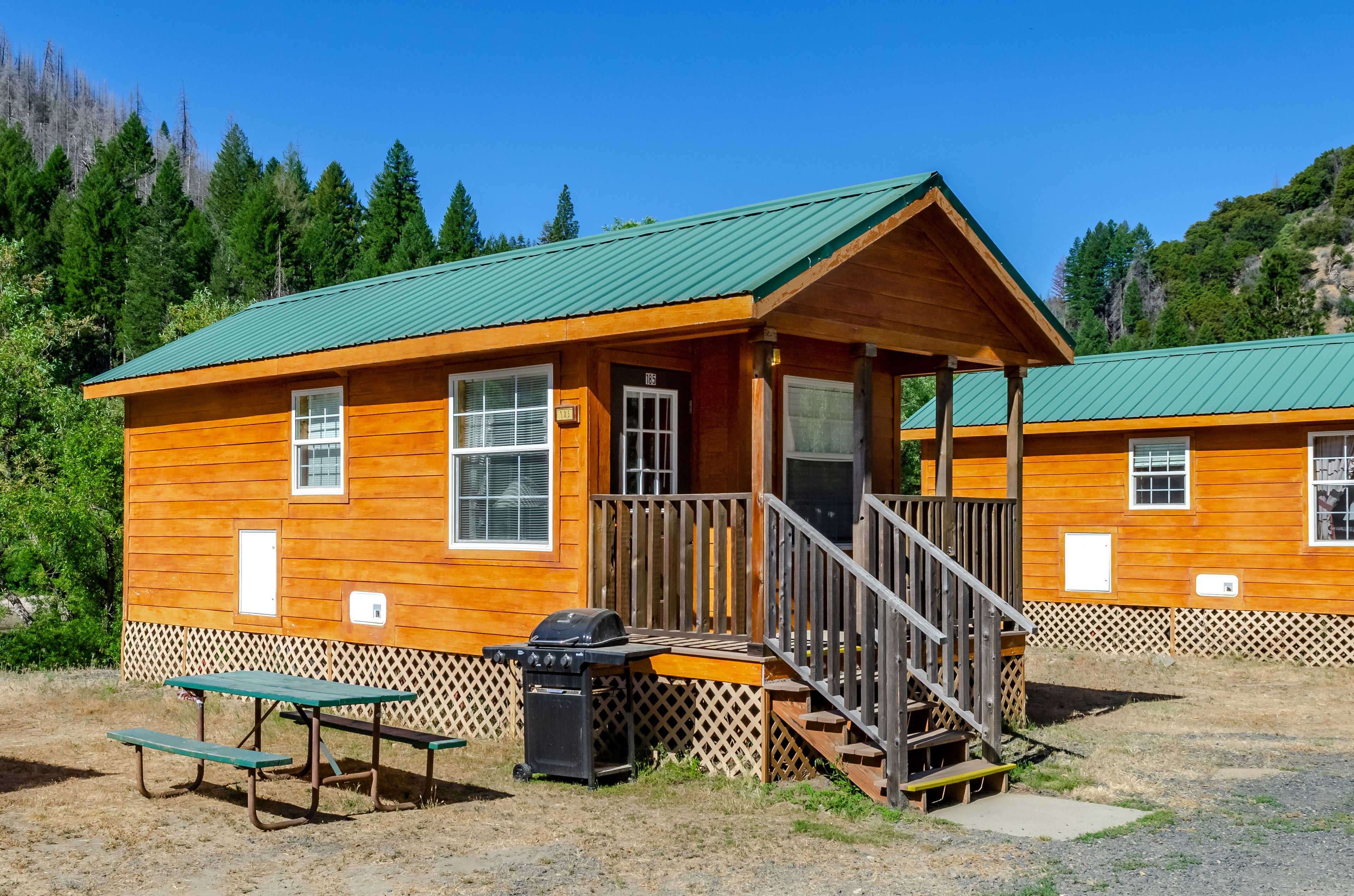 A wooden cabin with a green roof, a porch, and a picnic table.