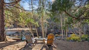 A campsite with two wooden Adirondack chairs, a concrete bench, and a small pond. - Yosemite Lakes RV Resort (Groveland)