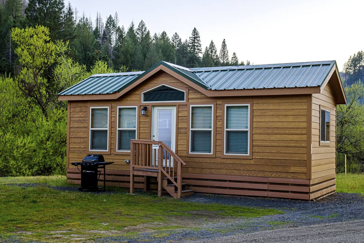 A wooden cabin with a metal roof, a front door, and a small porch with steps.