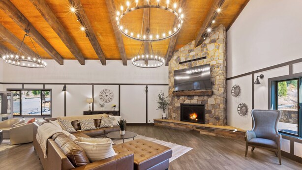 A spacious living room with a stone fireplace, leather sofa, and wooden beams on the ceiling. - Yosemite Lakes RV Resort (Groveland)