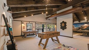 A cozy room with a foosball table, a dartboard, and a large window offering a view of trees. - Yosemite Lakes RV Resort (Groveland)