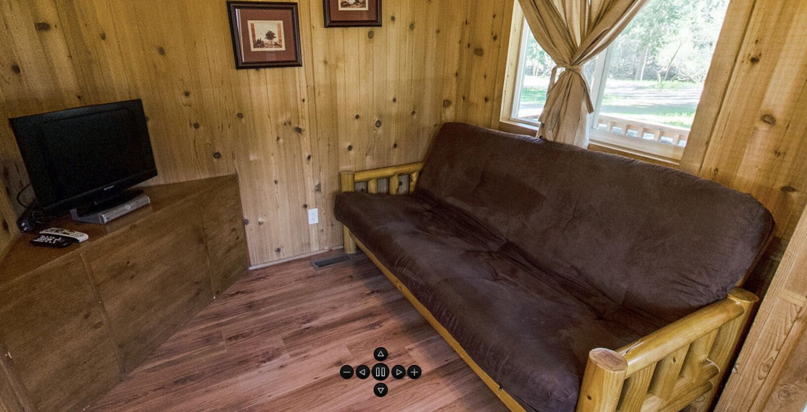 A wooden cabin interior with a brown sofa, a television, and framed pictures on the wall.