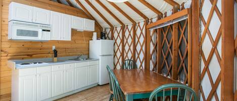 Cocina con armarios blancos, microondas y estufa. Hay una mesa de madera con sillas y una lámpara colgante.