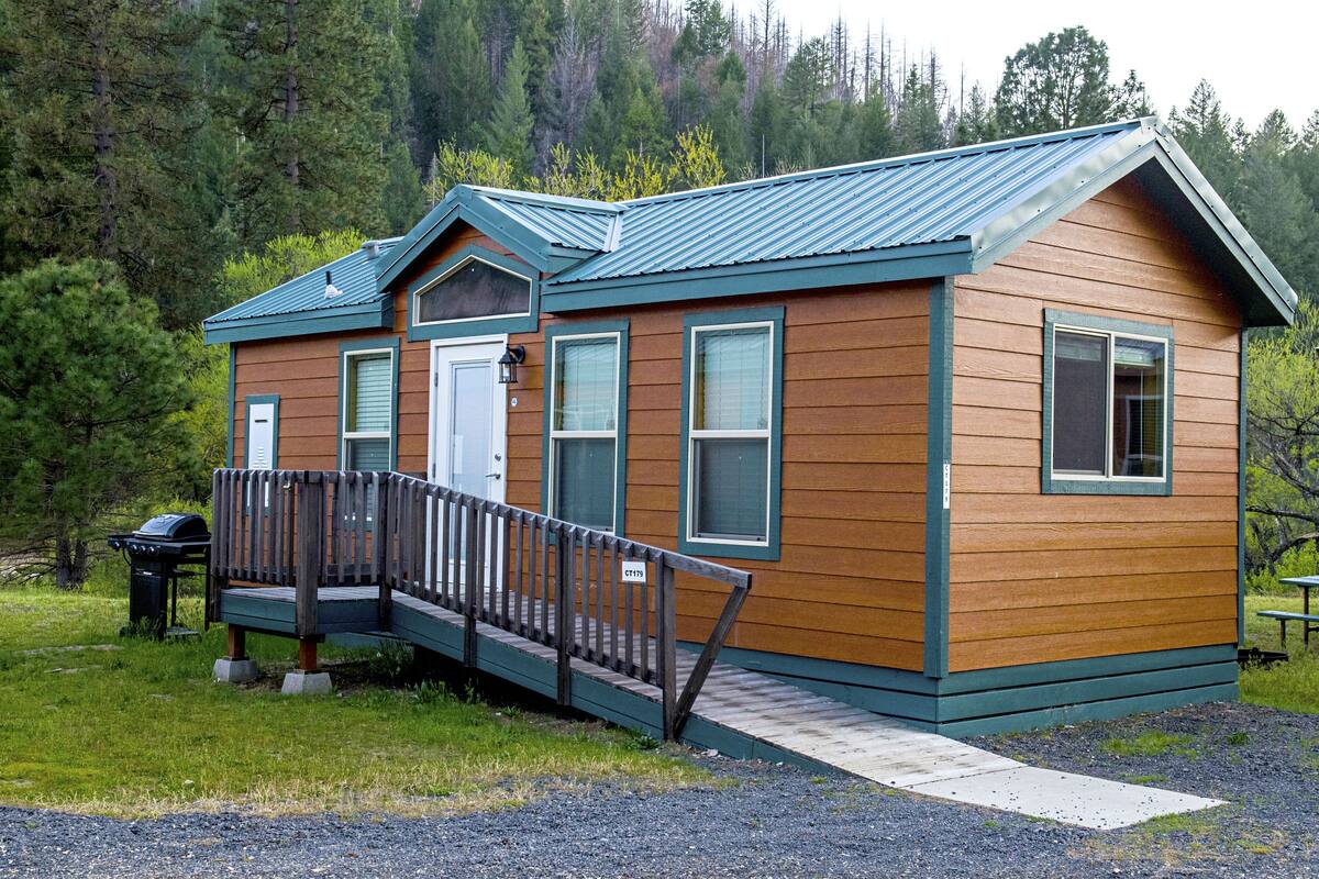 A small wooden cabin with a porch and a metal roof, surrounded by trees.