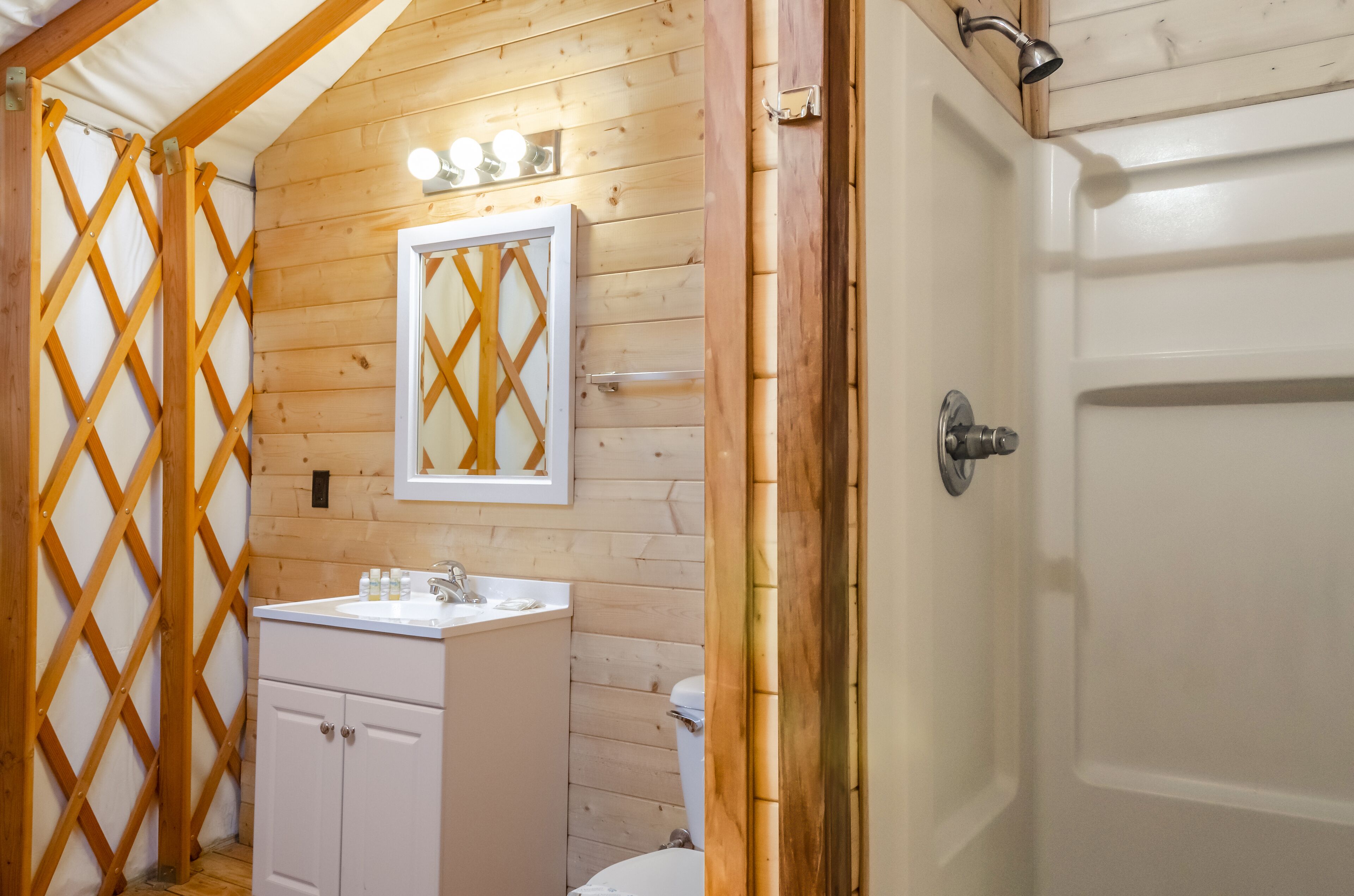 Une salle de bain aux murs lambrissés, équipée d’un lavabo, d’un miroir et d’une douche.