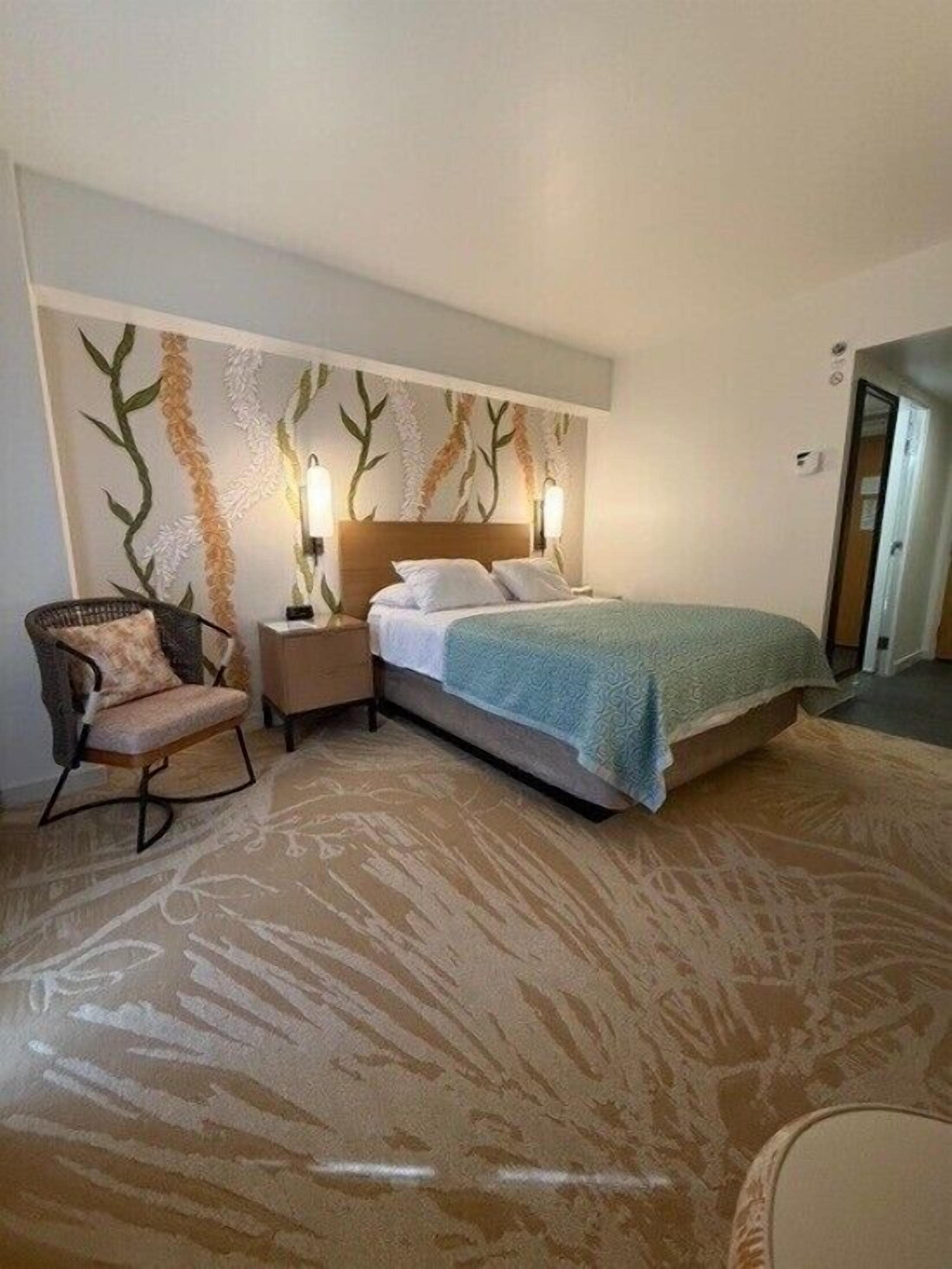 A hotel room with a bed, nightstands, a chair, and a patterned carpet.