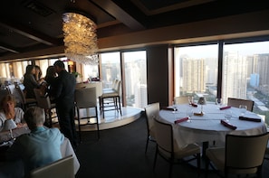 A restaurant with a high ceiling, large windows, and a view of tall buildings. - Ala Moana Hotel by LSI Resorts (Honolulu)