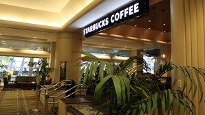 A Starbucks Coffee sign in a well-lit indoor area with seating and plants.