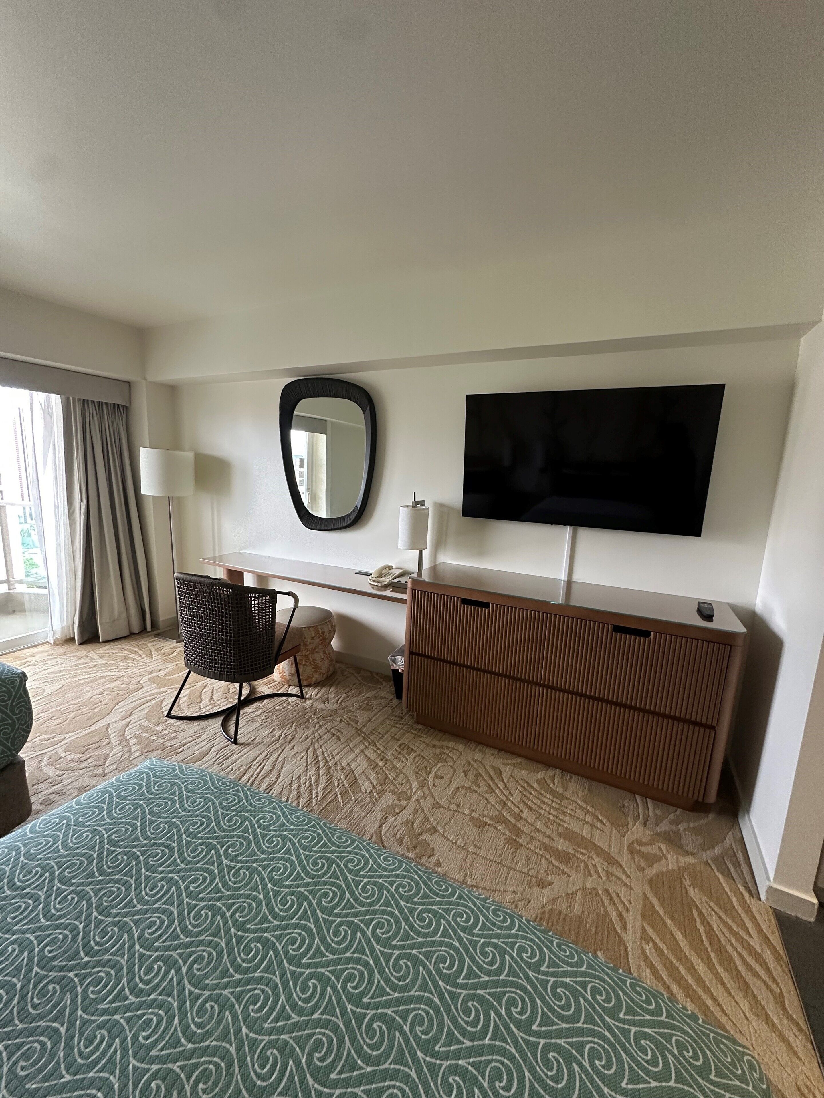 Une chambre d’hôtel avec un grand lit, un téléviseur fixé au mur, un bureau avec une chaise et une commode.