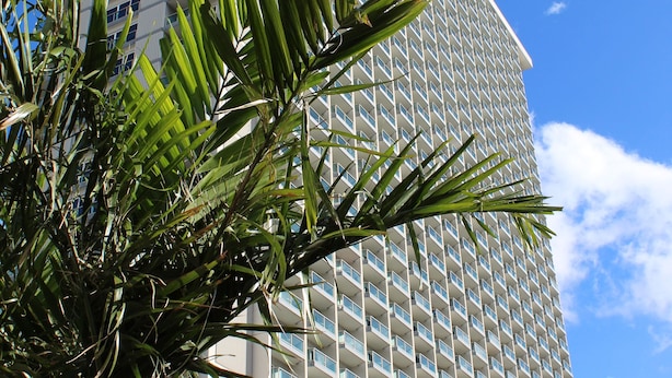 A tall hotel with a grid of balconies, surrounded by palm trees and a clear blue sky.