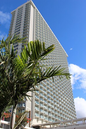 Un hotel alto con una cuadrícula de balcones, rodeado de palmeras y un cielo azul despejado.