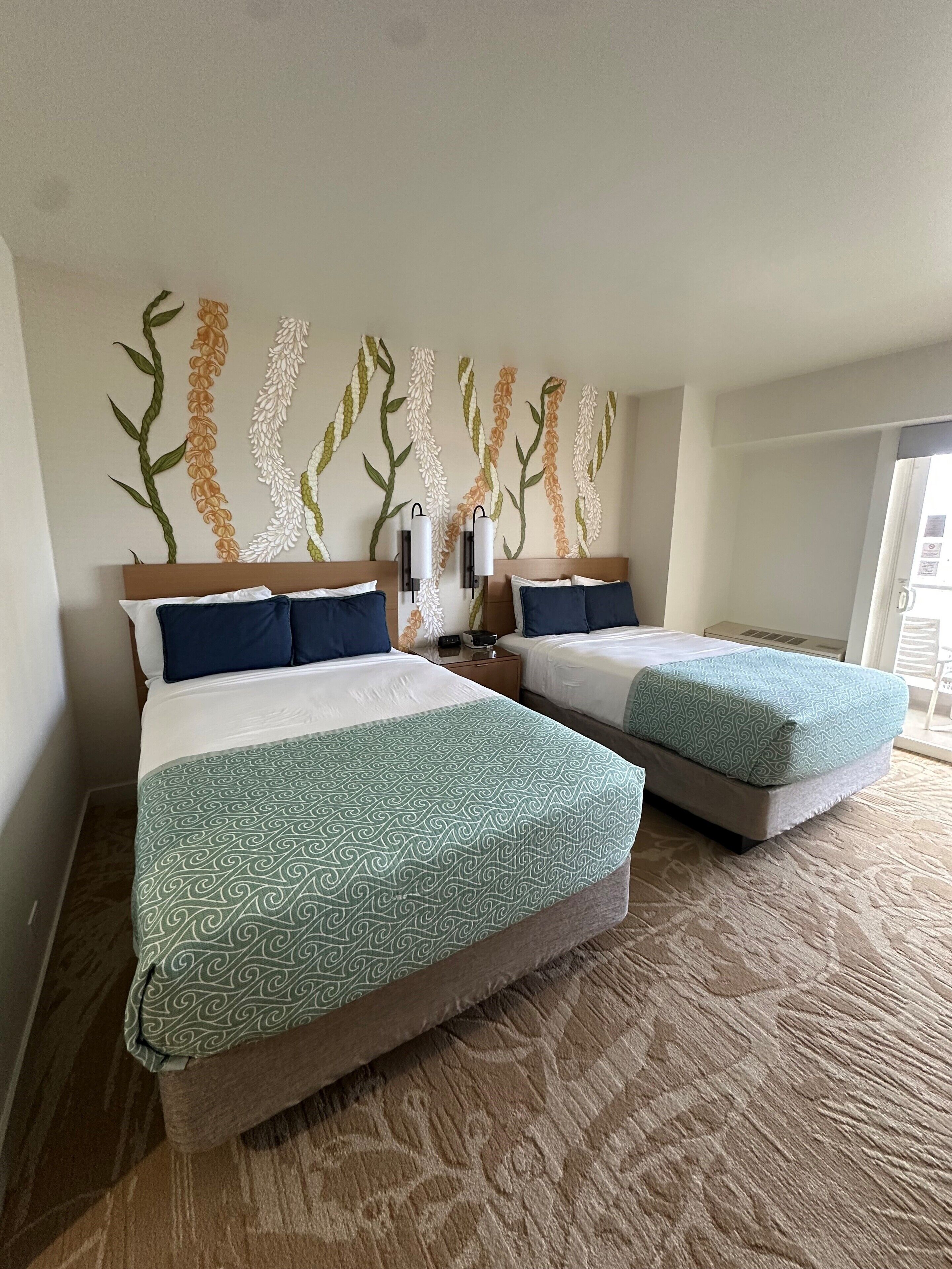 Een hotelkamer met twee bedden, een bed met een gestreept sprei, een muurschildering en een vloerkleed.