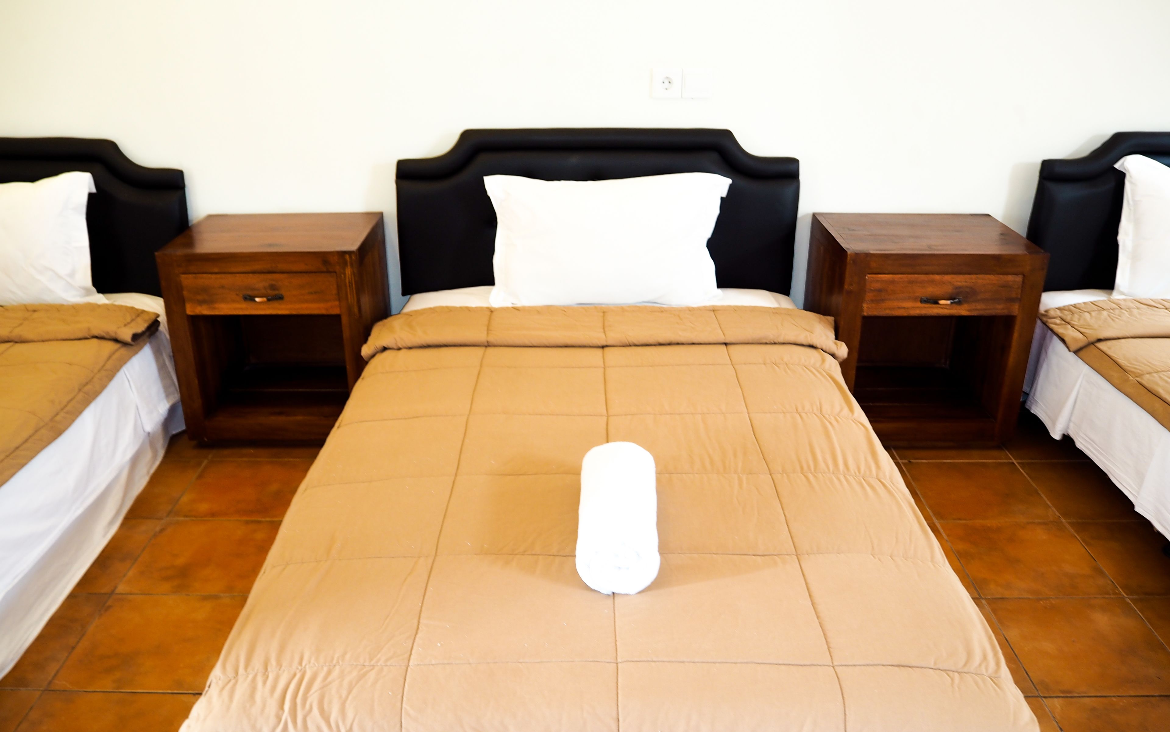 A neatly made bed with a white pillow and a brown bedspread in a hotel room.