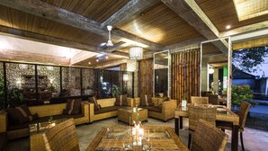 An outdoor seating area with wicker furniture and a glass-top table, featuring a bamboo wall and a ceiling fan. - Ecosfera Hotel (Canggu)