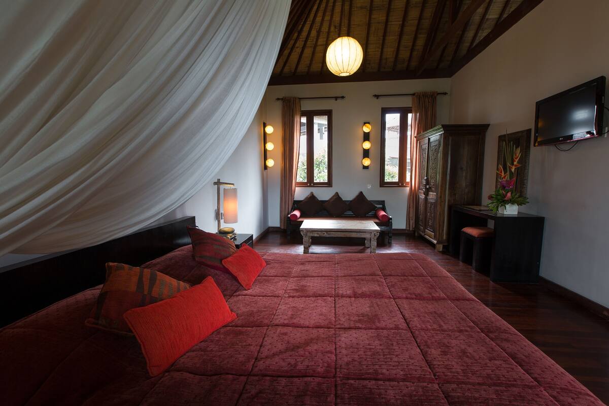 A spacious room with a large bed, a wooden ceiling, and a television on the wall.