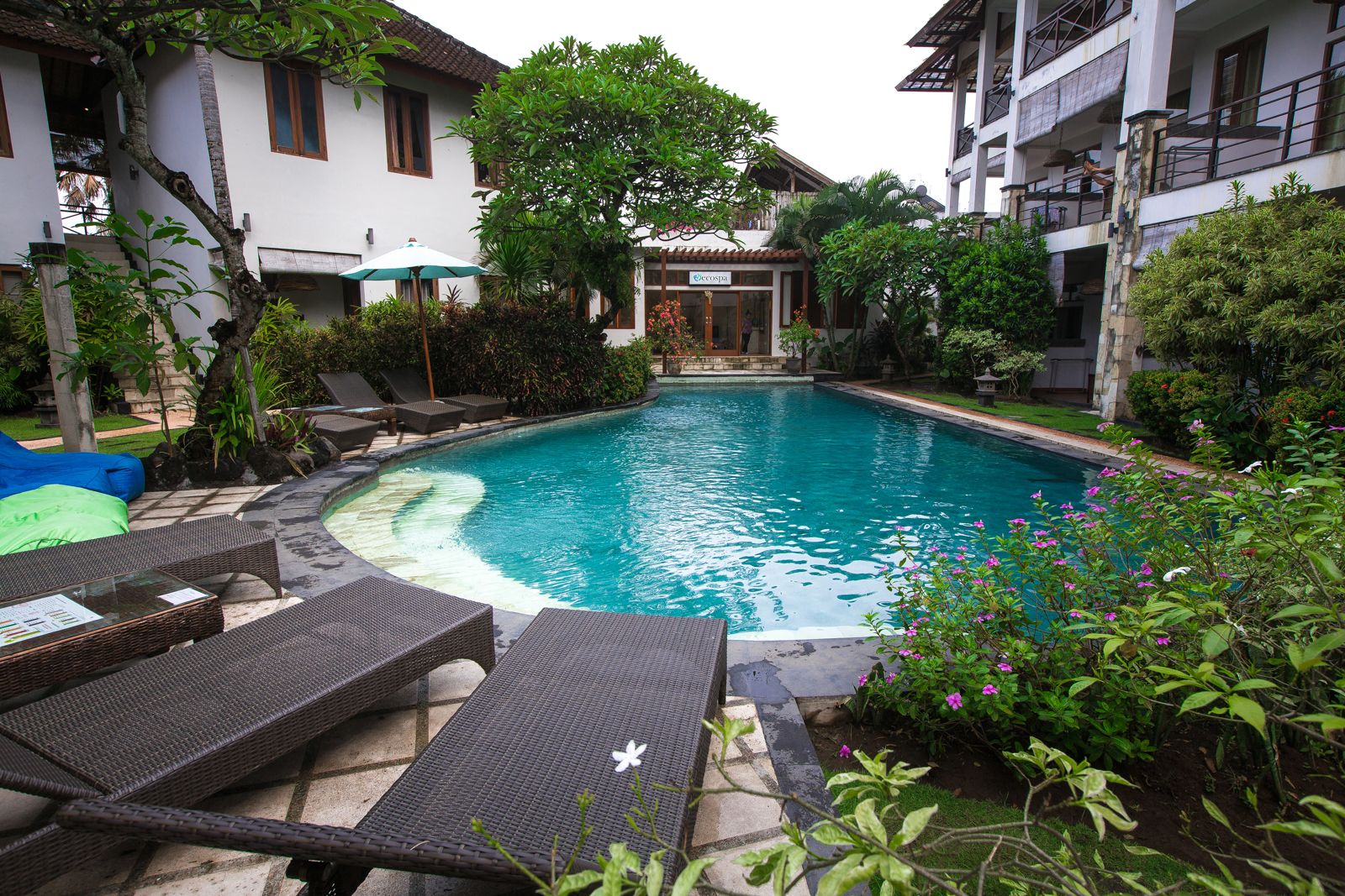 A swimming pool with lounge chairs, surrounded by greenery and a building with a spa sign.