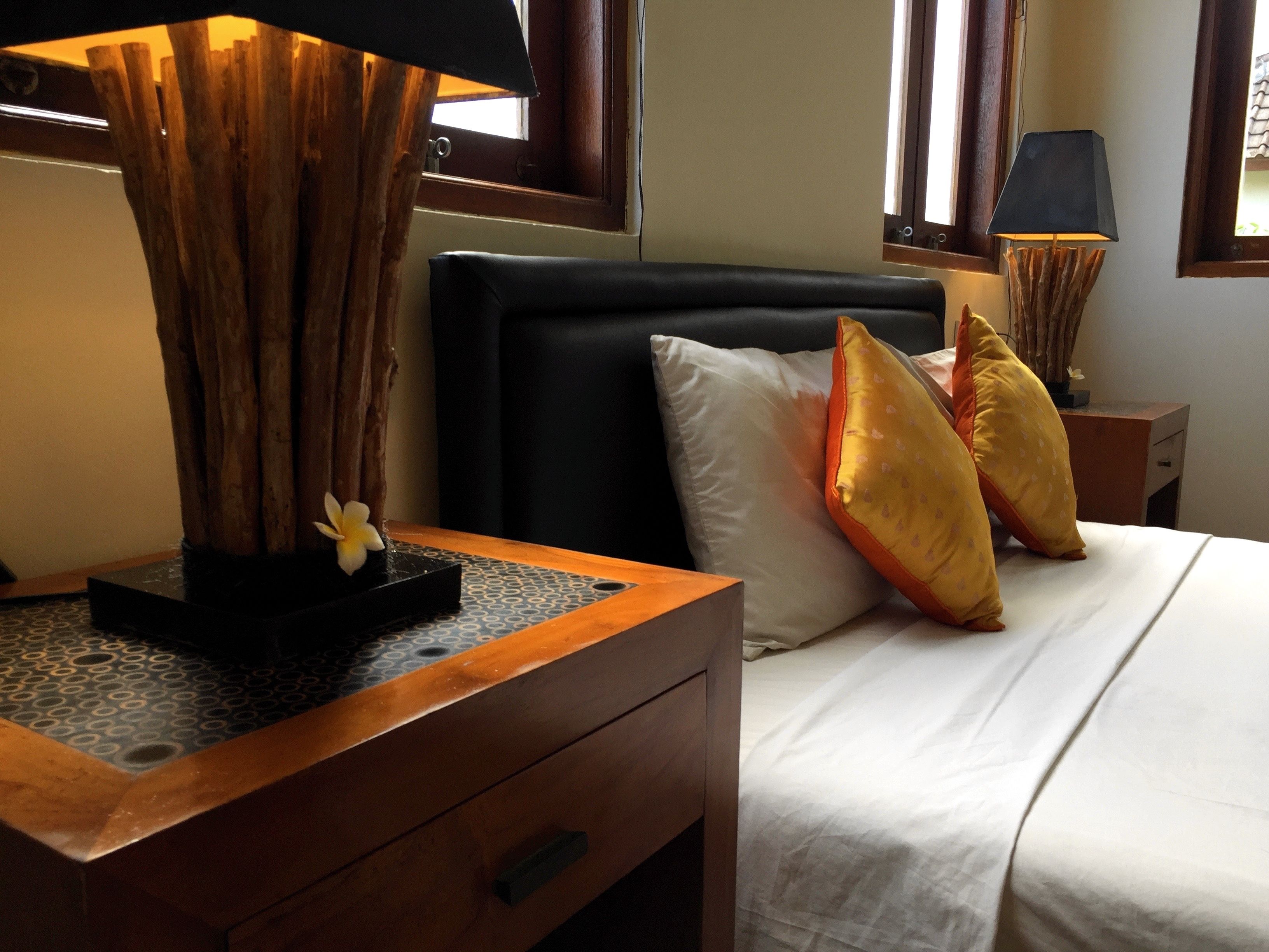 A hotel room with a bed, a wooden nightstand, a lamp, and a window with curtains.