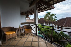 Un balcón con mobiliario de mimbre y vista a una zona residencial con palmeras.