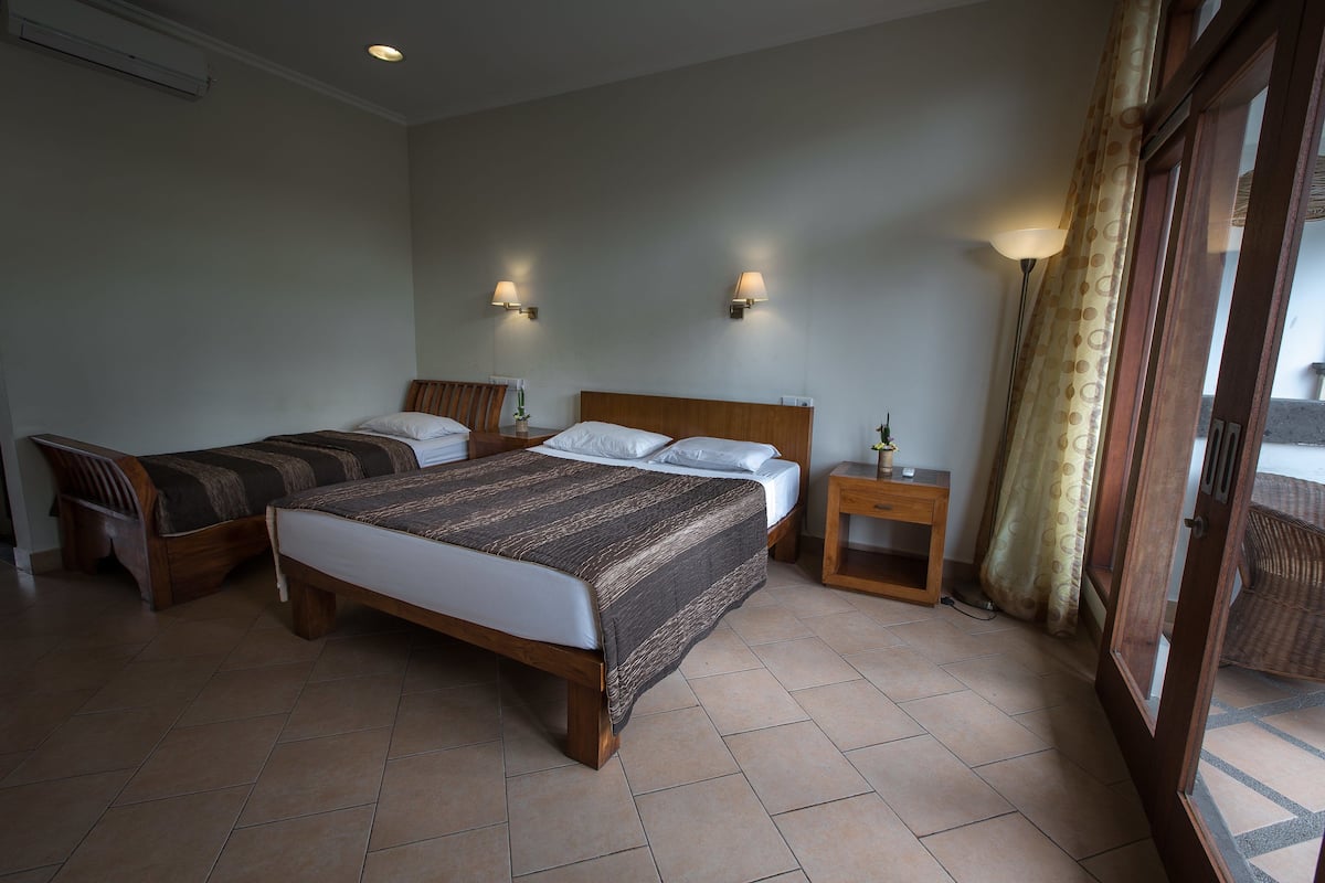 A hotel room with two single beds, a wooden headboard, a nightstand, a lamp, and a window with curtains.