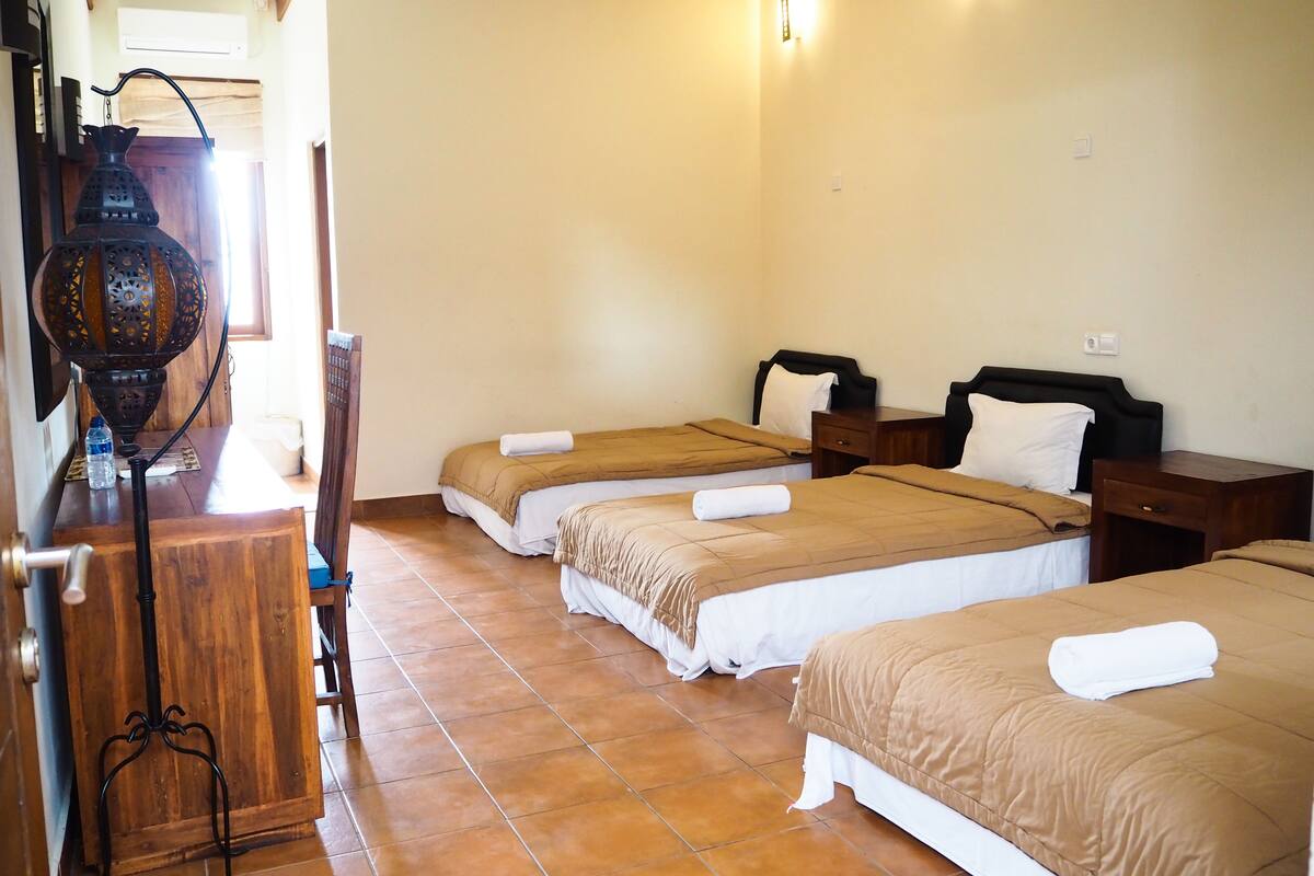 A hotel room with three beds, a wooden desk, a decorative lantern, and a tiled floor.