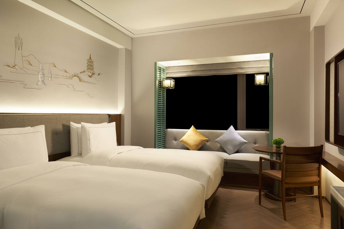 A hotel room with two beds, a desk, and a chair.