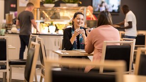 A restaurant with wooden chairs and tables, a counter with a person serving, and a TV screen in the background. - Mawson Lakes Hotel & Function Centre (Mawson Lakes)