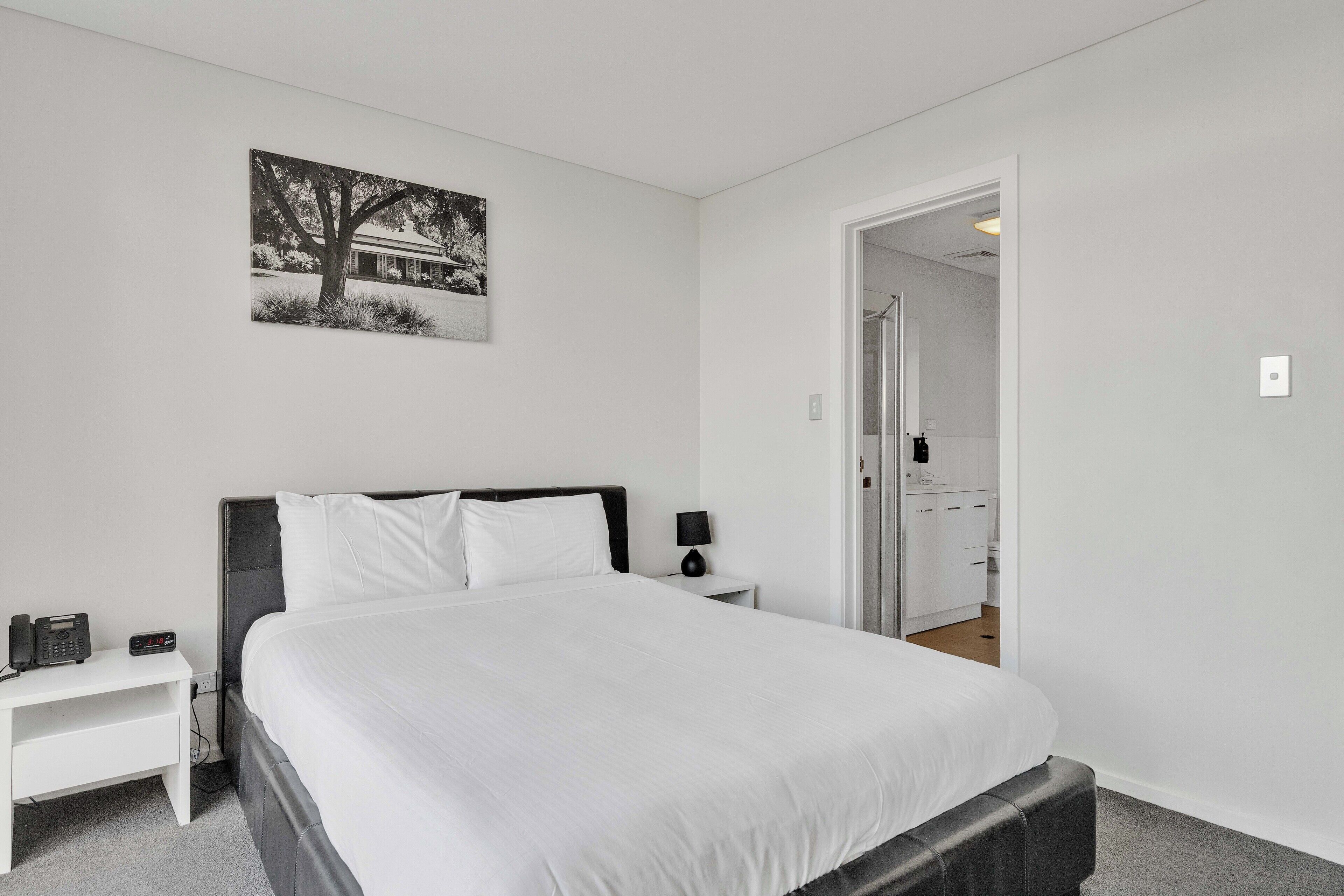 A bedroom with a bed, bedside table, lamp, and a painting on the wall.