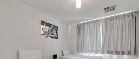 Een hotelkamer met twee bedden, een nachtkastje met een lamp, een raam met gordijnen en een aan de muur bevestigd schilderij.
