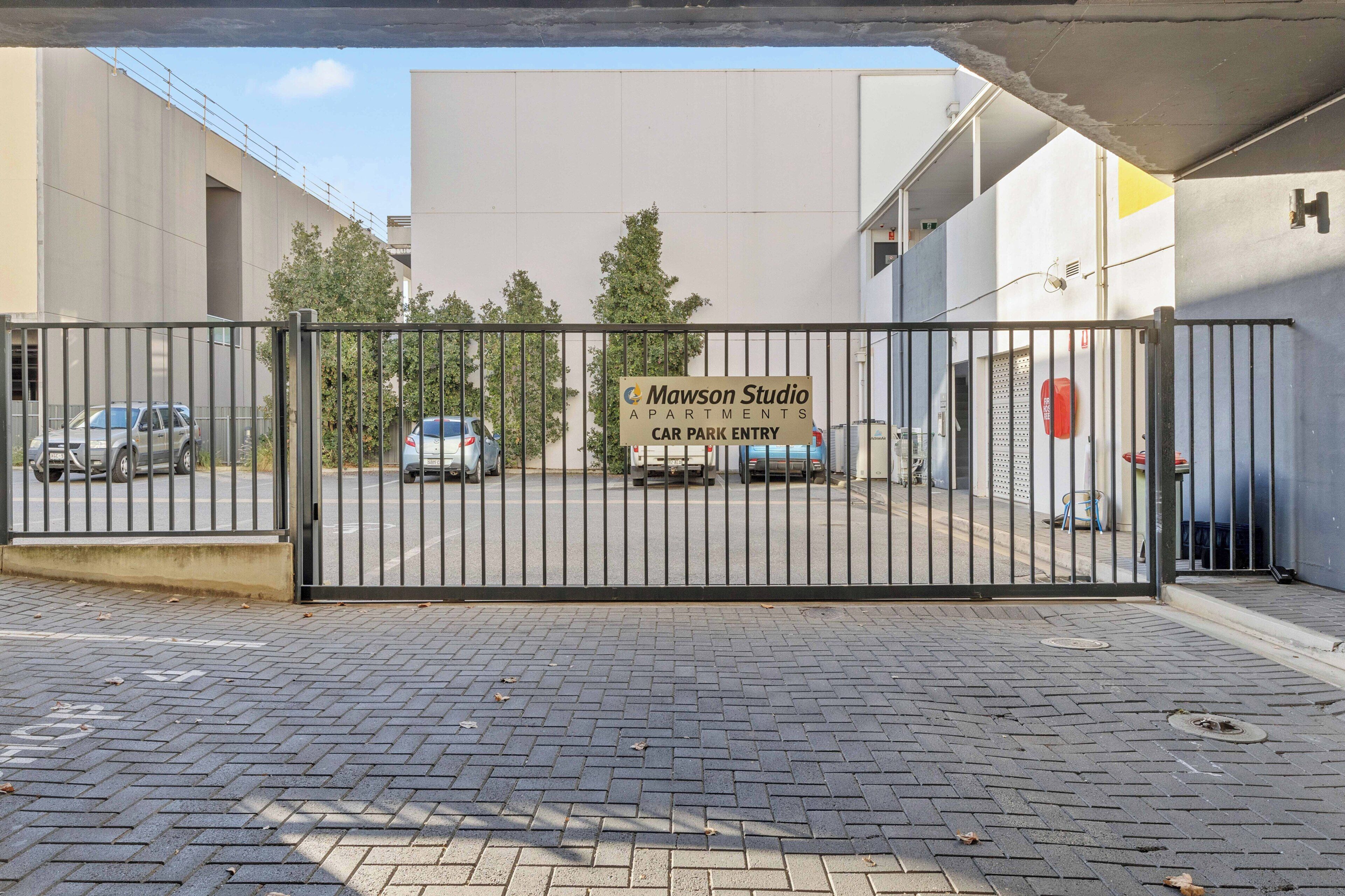 A gated entrance to a building with a sign indicating 'Mawson Studio Apartments Car Park Entry.'