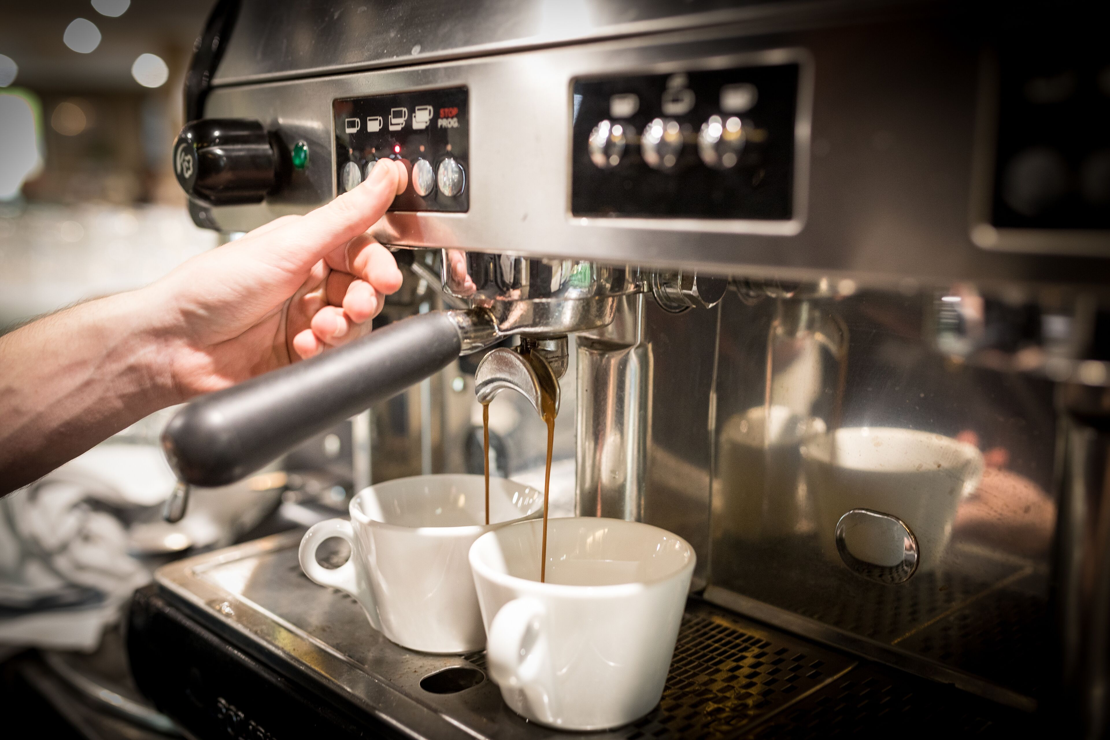 Una mano ajustando una máquina de café espresso, con dos tazas debajo.