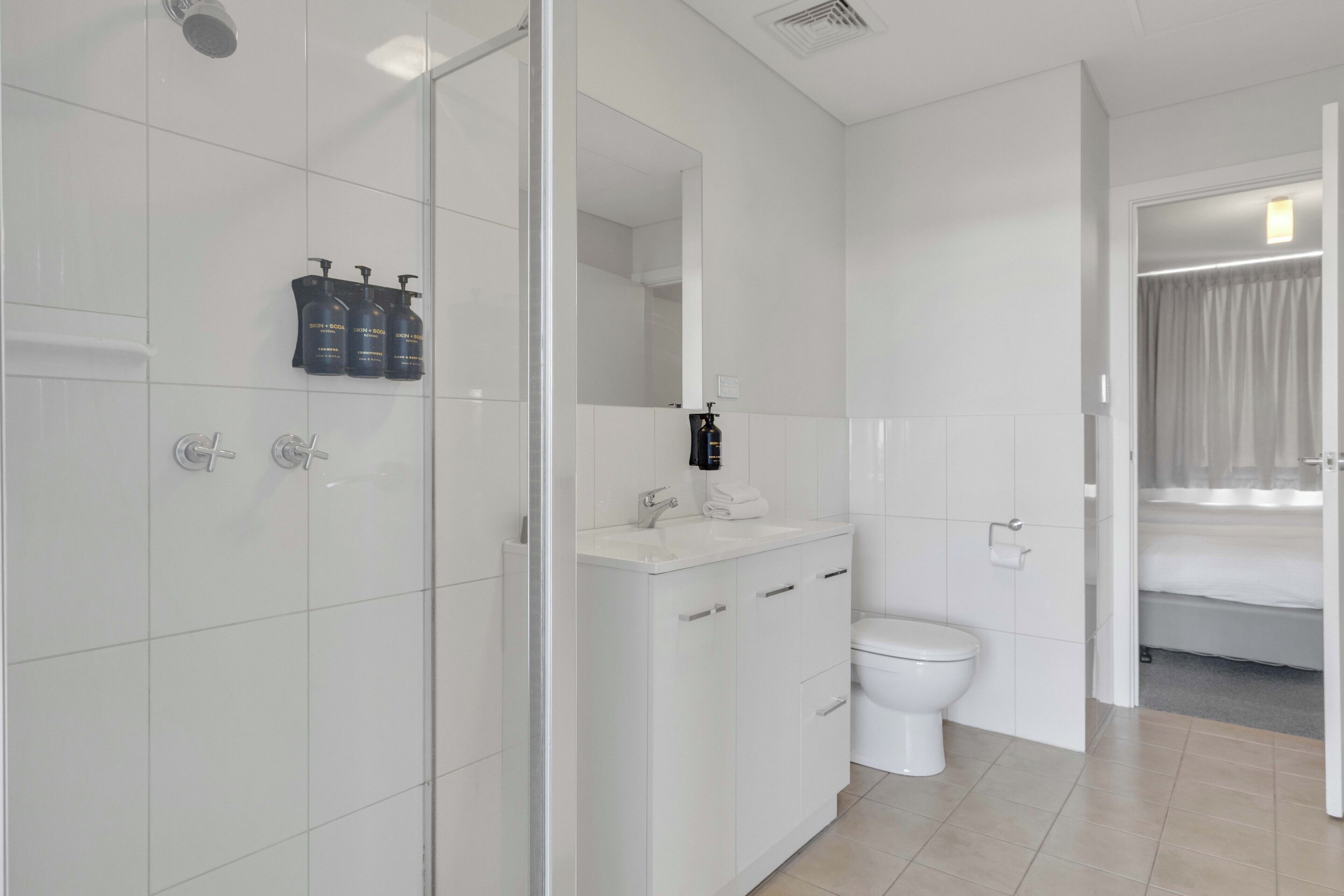 A modern bathroom with a glass shower enclosure, a white sink with a mirror, and a toilet.