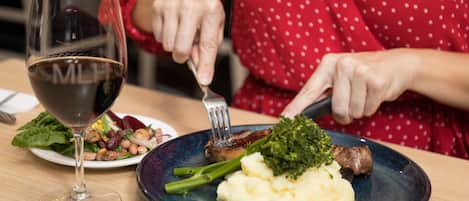 A dining table with a plate of food, a glass of red wine, and a person cutting meat.