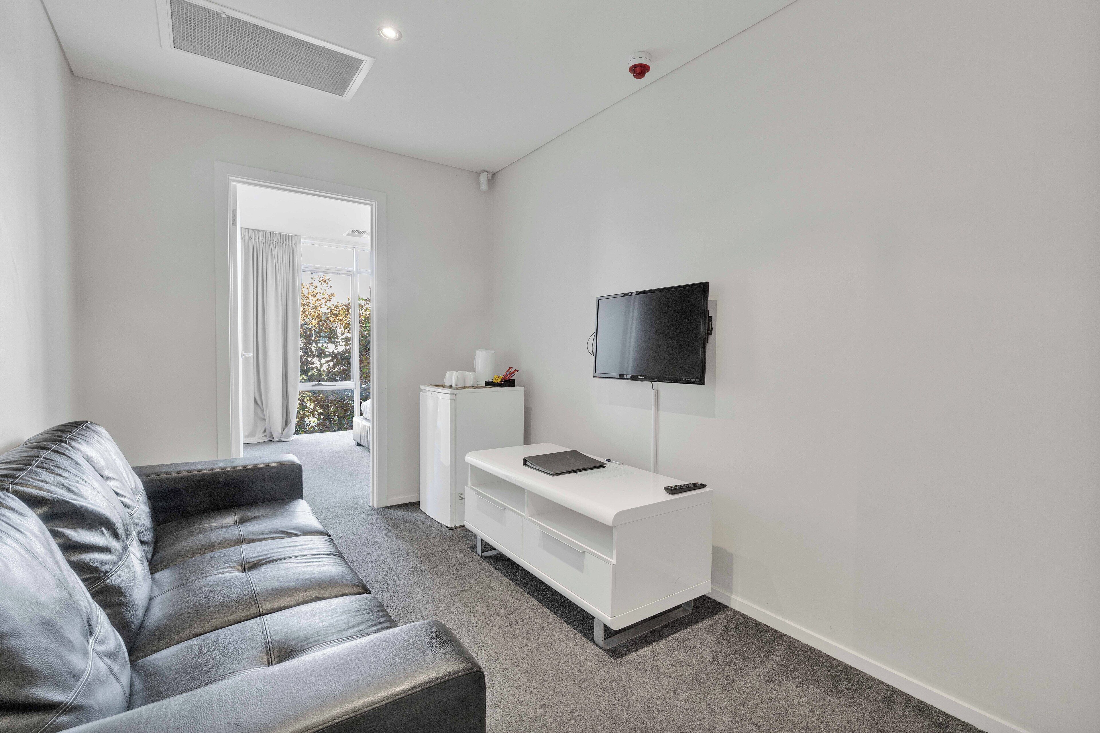 A modern living room with a leather sofa, a white entertainment unit, and a mounted TV.
